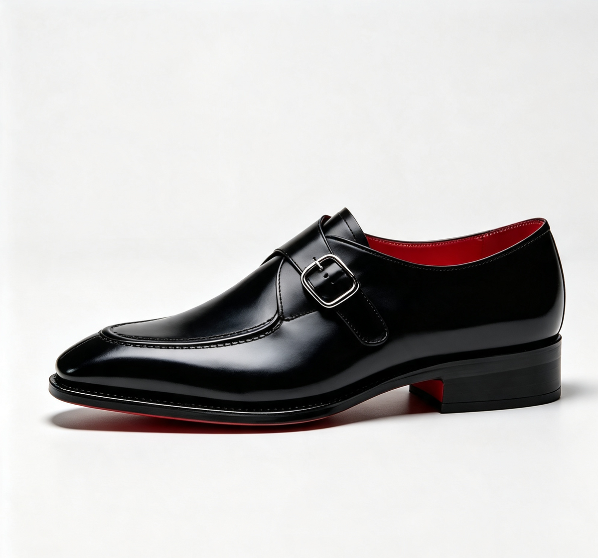 A black leather double monk shoe with a silver buckle, shown from a side profile on a light gray background. The shoe features a glossy finish, a low stacked heel, and a contrasting red outsole visible at the heel and inner side.